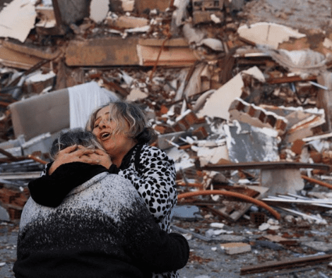 Una donna abbraccia un apersona piangendo davanti alle case distrutte