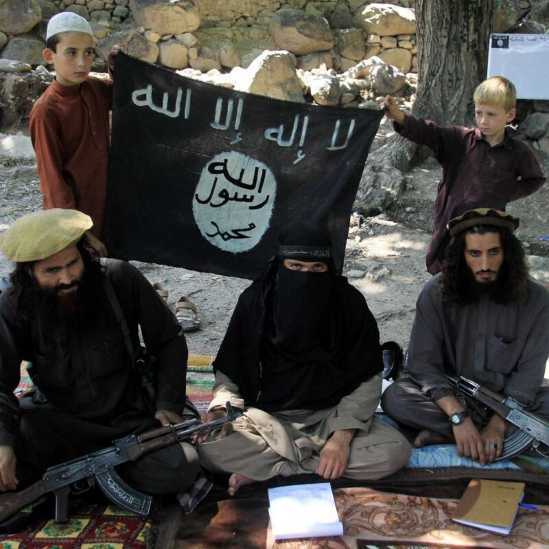 Miliziani armati con bandiera ISIS durante un raduno jihadista in zona di conflitto
